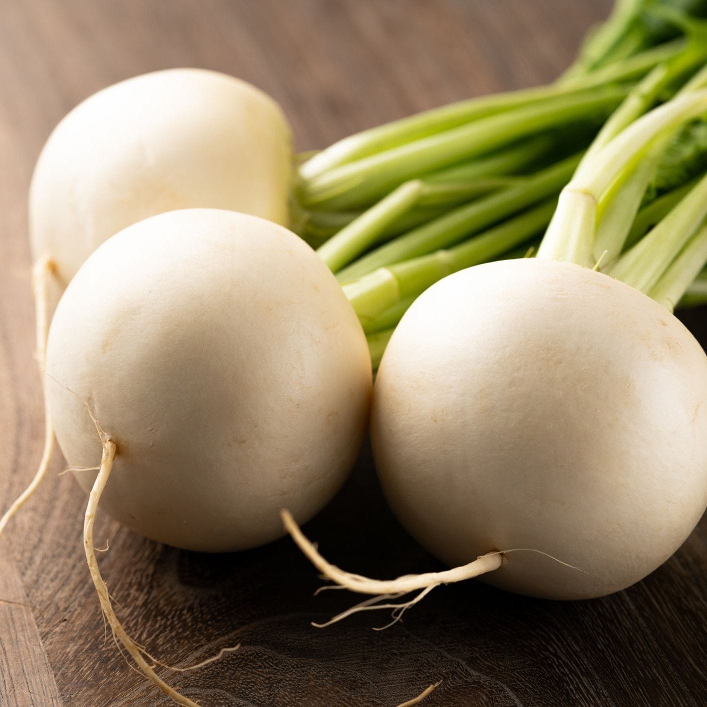 Three white turnips with green tops on a wooden surface