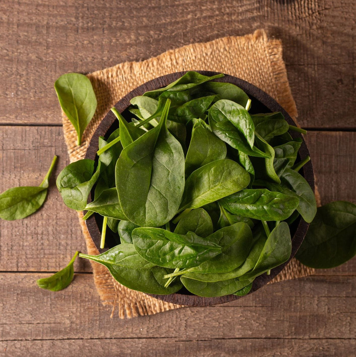Bowl of fresh spinach leaves on a wooden surface