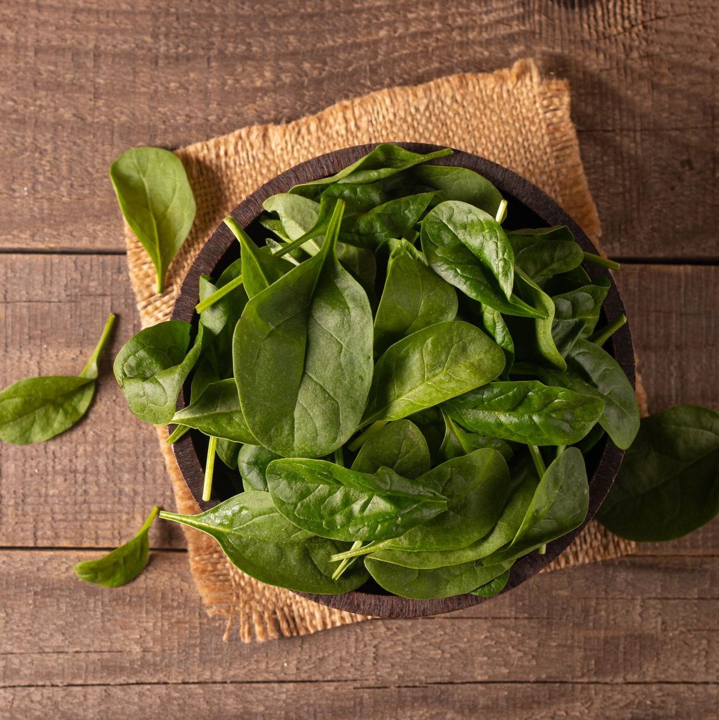 Bowl of fresh spinach leaves on a wooden surface